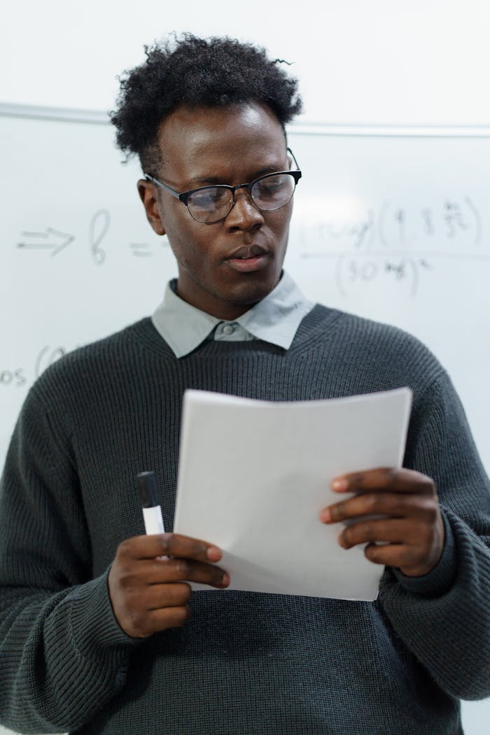 Elegantly Dressed Man Holding Paper and Standing in front of a Board 